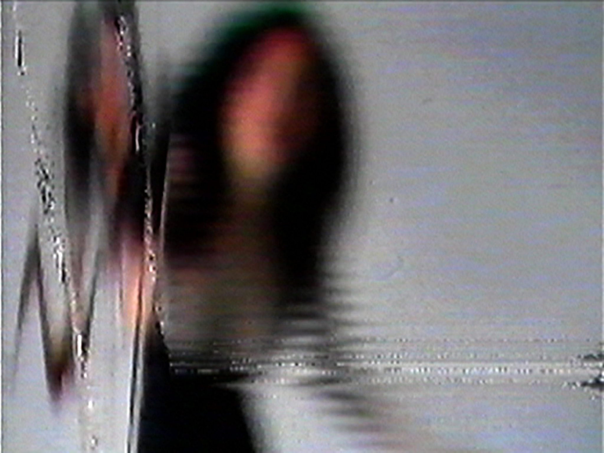 A blurred figure stands against a light background, partially distorted by horizontal lines and digital noise, giving the image a glitchy, abstract effect.